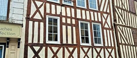 Un edificio tradicional con entramado de madera y varias ventanas, con una furgoneta blanca estacionada adelante.