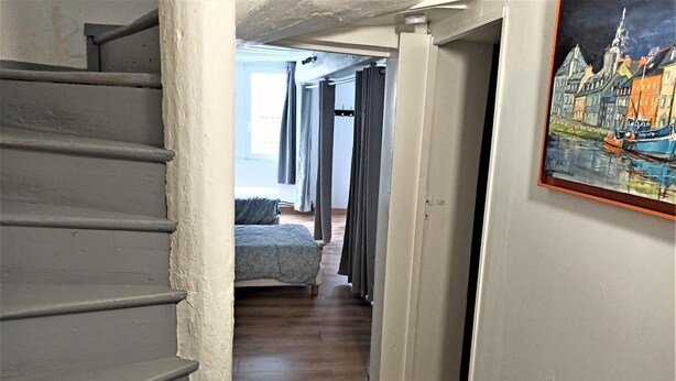 Un pasillo estrecho con una escalera que lleva a un dormitorio con cama y cortinas.