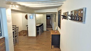 Un pasillo con suelo de madera, una zona de comedor con sillas y una mesa, y un perchero en la pared.