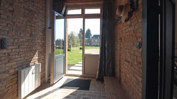 A narrow hallway with a wooden ceiling and brick walls, leading to a glass door opening to a lawn. - Gîtes de France® - The Orangery (HUGLEVILLE EN CAUX)