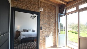 A bedroom with a bed, a nightstand, a lamp, and a brick wall. - Gîtes de France® - The Orangery (HUGLEVILLE EN CAUX)