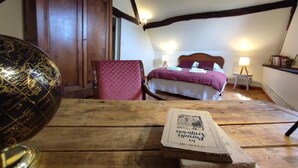 Ein gemütliches Schlafzimmer im Dachgeschoss mit Holzbalkendecke, einem Bett mit lila Bettdecke, einem Globus und einer Zeitung auf dem Boden.