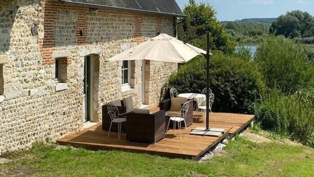 Ein Gebäude aus Stein mit einer Holzterrasse und Sitzgelegenheiten im Freien.