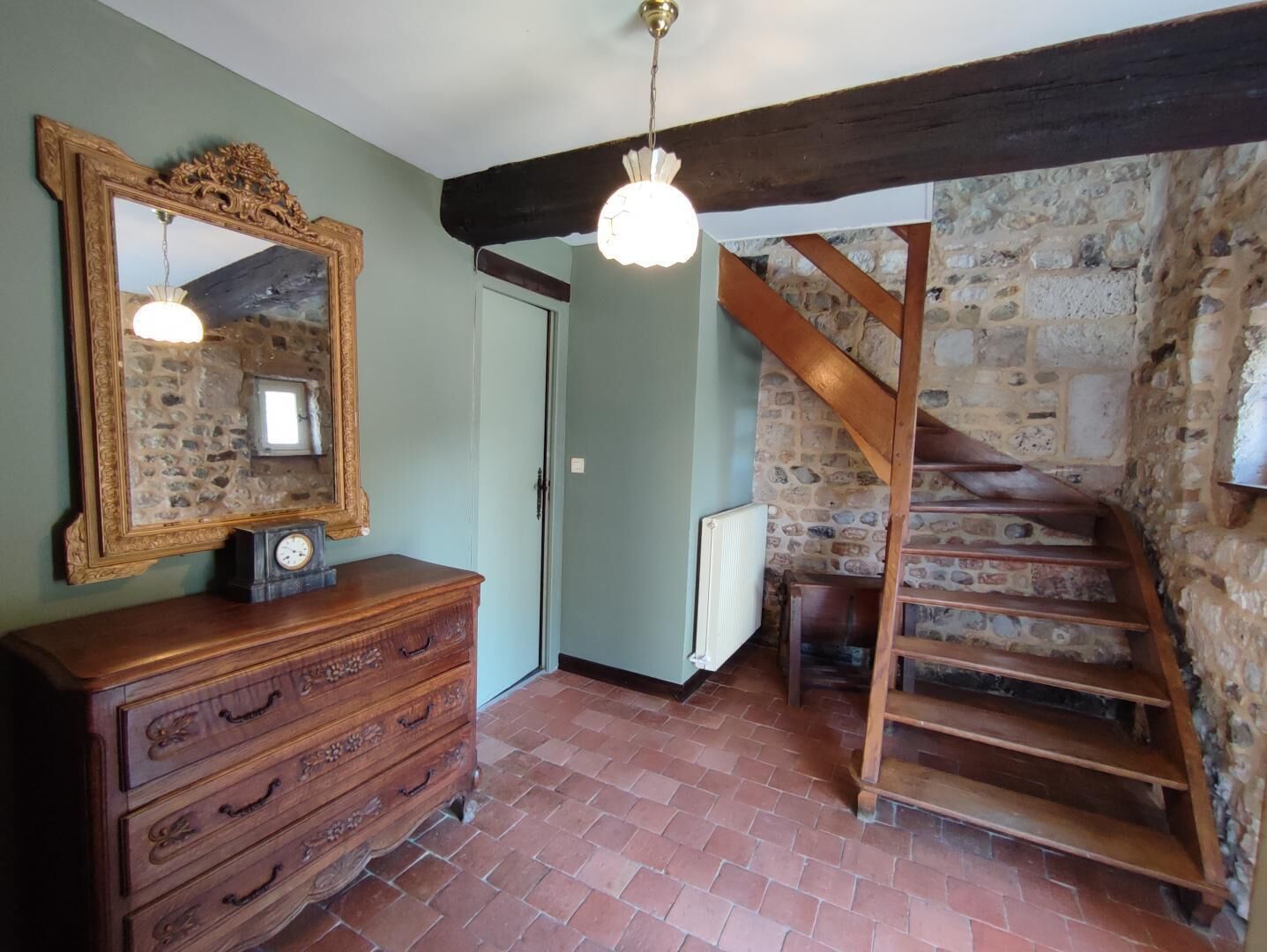 A room with a stone wall, a wooden staircase, a dresser with drawers, a mirror, and a hanging light fixture.