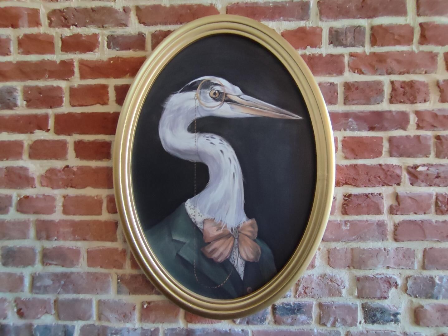 A framed painting of a bird on a brick wall.