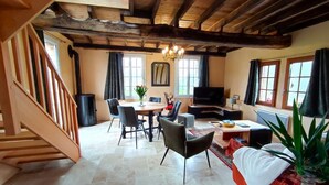 Amplia sala de estar con escalera de madera, mesa de comedor con sillas, sofá, televisor y chimenea.