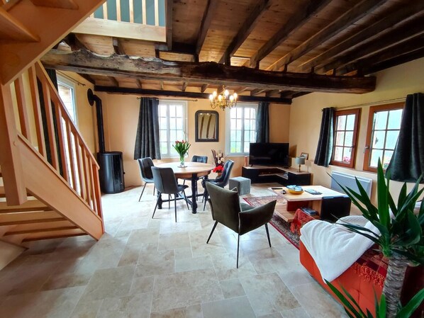 Amplia sala de estar con escalera de madera, mesa de comedor con sillas, sofá, televisor y chimenea.