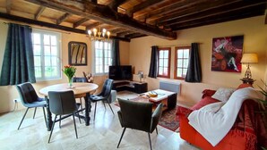 Una sala de estar con techo de madera, una mesa redonda de comedor con sillas, un sofá, un televisor y un cuadro en la pared.