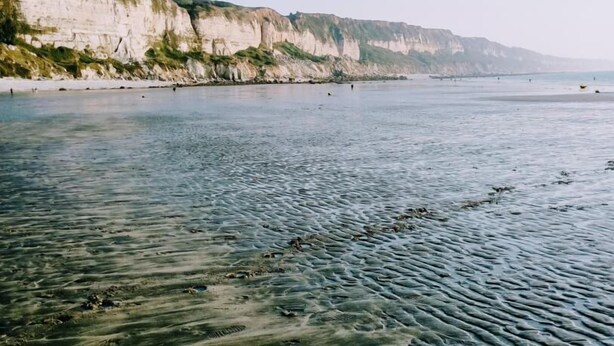 Una playa con aguas cristalinas poco profundas y un acantilado al fondo.