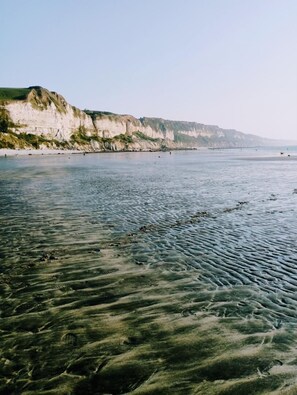 Una playa con aguas cristalinas poco profundas y un acantilado al fondo.