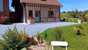 Una casa tradicional con entramado de madera y tejado inclinado, camino de grava y jardín bien cuidado con diversas plantas y flores.