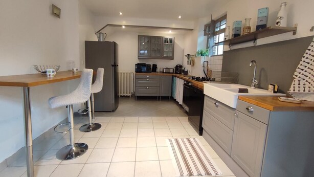 A modern kitchen with a bar area, stainless steel appliances, and a tiled floor. - Gîtes de France® - Gîte du Dun (FONTAINE LE DUN)