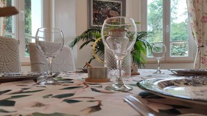 A dining table set with glassware and plates, surrounded by chairs with a floral pattern. - Gîtes de France® - Gîte du Dun (FONTAINE LE DUN)