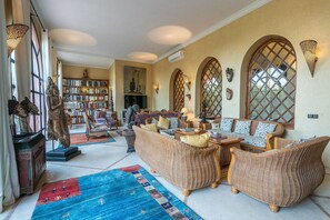 A spacious living room with wicker furniture, a bookshelf, and decorative items. - Luxury villa, pool, spa and 5-star sercice (Makinat Sridi)