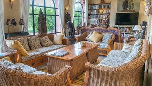 A spacious living room with wicker furniture, a bookshelf, and a large window with a view of greenery. - Luxury villa, pool, spa and 5-star sercice (Makinat Sridi)