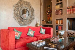 A red sofa with patterned cushions, a decorative mirror, and a bookshelf with books and decorative items.