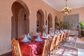 A dining area with a long table set for a meal, featuring traditional table settings and a decorative wall with intricate patterns.