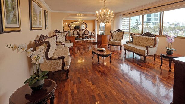 A spacious living room with hardwood flooring, elegant furniture, and large windows offering a city view.