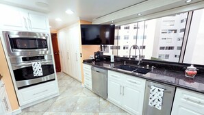 A modern kitchen with stainless steel appliances, a flat-screen TV, and a large window with a city view.