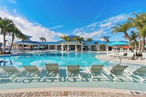 A swimming pool with lounge chairs, palm trees, and a building with a blue roof.