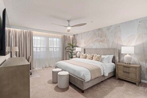 A bedroom with a large bed, bedside tables, a ceiling fan, and a view of the outdoors through the window.