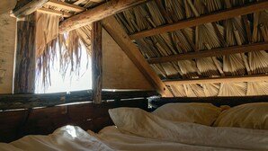 Een rustieke kamer met een houten plafond, een bed met wit beddengoed, en een raam waardoor natuurlijk licht binnenkomt.