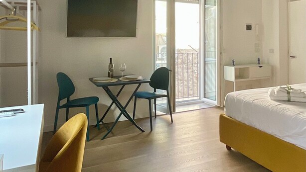 Een kamer met een bed, een eettafel met stoelen, een televisie en een balkon met een hekwerk.