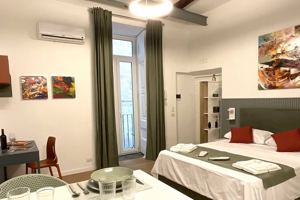 Une chambre d’hôtel avec un lit, une table à manger avec des assiettes et des couverts, une chaise verte et un tableau accroché au mur.