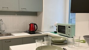 Een moderne keuken met grijze kastjes, een wit aanrecht, een rode waterkoker, een broodrooster en een raam met zonwering.