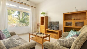 Una sala de estar con un sofá, una mesa de centro, un televisor y un mueble de madera con puertas de cristal.