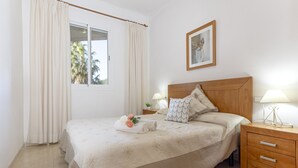 Un dormitorio con cama, dos mesitas de noche, una lámpara de noche, una ventana con cortinas y un cuadro en la pared.