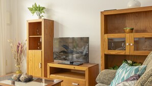 Una sala de estar con un mueble de madera, un televisor sobre un pedestal, un sofá y una pequeña mesa con objetos decorativos.
