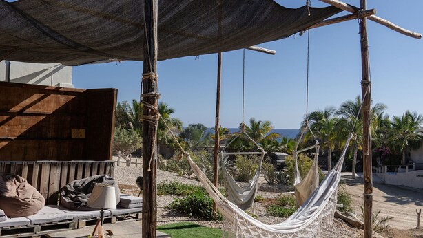 A hammock under a shaded area, wooden lounge chairs, and a view of the ocean. - The Baja Station - Palapa in front of the surf break (San José del Cabo)
