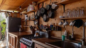 A rustic kitchen with wooden cabinets, a stove, and various kitchen utensils and appliances. - The Baja Station - Palapa in front of the surf break (San José del Cabo)