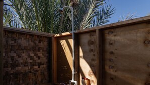 A wooden outdoor shower enclosure with a woven privacy screen, a metal showerhead, and two bottles on a shelf. - The Baja Station - Palapa in front of the surf break (San José del Cabo)