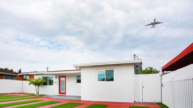 Una casa moderna con puerta roja, cerca blanca y césped cuidado.
