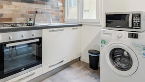 Une cuisine compacte avec un mur de fond en briques, un four encastré, un four à micro-ondes et un lave-linge.