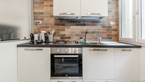 Une cuisine avec un mur de fond en briques, des appareils électroménagers en acier inoxydable et des meubles de cuisine blancs.