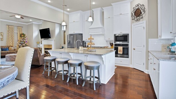 A modern kitchen with white cabinetry, a central island with stools, and a dining area with a table and chairs. - Southern Comfort! Charming 3 Bedroom Between Baton Rouge and New Orleans (Geismar)