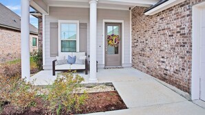 A residential house with a covered porch, a brick exterior, and a front door with a wreath. - Southern Comfort! Charming 3 Bedroom Between Baton Rouge and New Orleans (Geismar)
