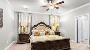 A bedroom with a large bed, two nightstands, a ceiling fan, and a door. - Southern Comfort! Charming 3 Bedroom Between Baton Rouge and New Orleans (Geismar)