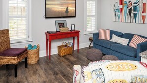 A cozy living room with a blue sofa, wicker chair, and a red table with a television above.