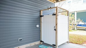 A grey exterior wall with a white door, a blue and white doormat, and a wooden structure near the door.