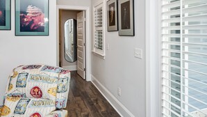 A hallway with a patterned armchair, framed artwork on the walls, and a door leading to another room.