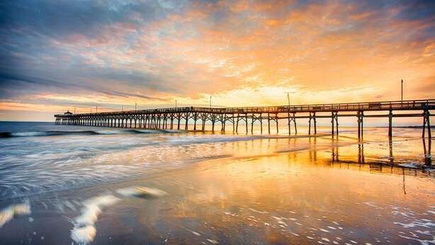 A pier extending into the sea with a sunset in the background.