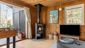 A cozy living room with a wood-burning stove, a foosball table, a flat-screen TV, and a large window offering a view of trees. - Gorgeous home in Vejby with WiFi (Vejby)