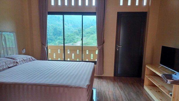 Une chambre avec un grand lit, une télévision, une porte et un balcon donnant sur un paysage verdoyant.
