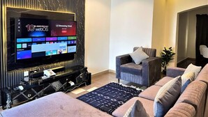 Ein modernes Wohnzimmer mit einem großen Flachbildfernseher, einem grauen Sofa und einem gemusterten Teppich.
