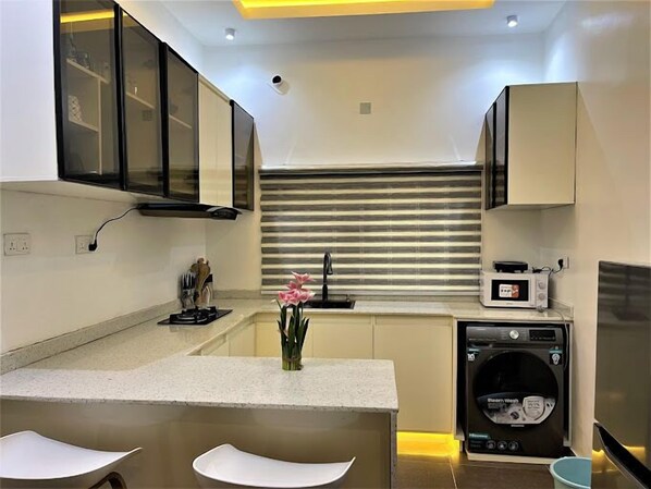 A compact kitchen with a built-in microwave, a coffee machine, and a washing machine. - Skyview Homes (Abuja)