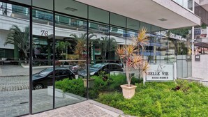 A modern building with glass windows reflecting the surroundings. There is a sign for 'Belle Vie Residence' and another for 'Solange Imóveis'.